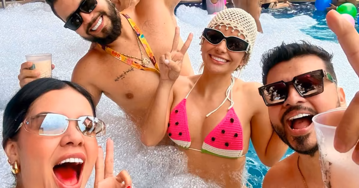 Four friends in sunglasses and swimwear flash peace signs, laughing by the bubbly pool at Coco Bongo Beach Club.