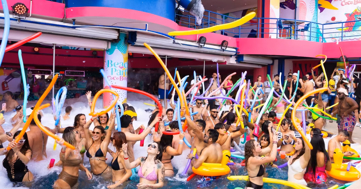 People in swimwear dance and play with balloons at a colorful, festive pool party at Coco Bongo Beach Club.