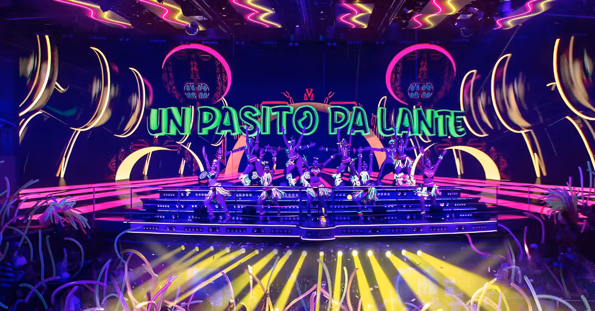 Colorful stage at Coco Bongo Night Club with neon lights, performers, and glowing UN PASITO PA LANTE text among lively decor.