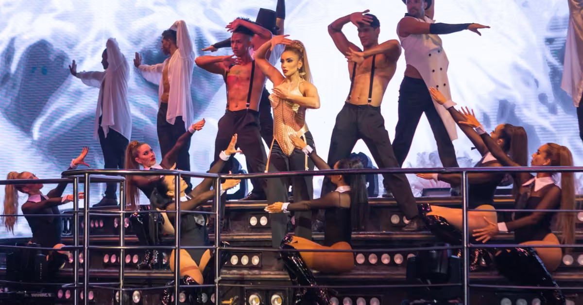 Dancers perform on stage at Coco Bongo, with a central woman striking a pose as others move around her on lit-up steps.