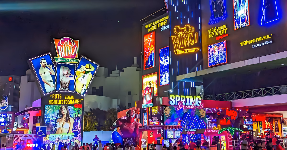 Colorful neon signs and lively crowds fill the bustling city night, with Coco Bongo lit up among glowing billboards.
