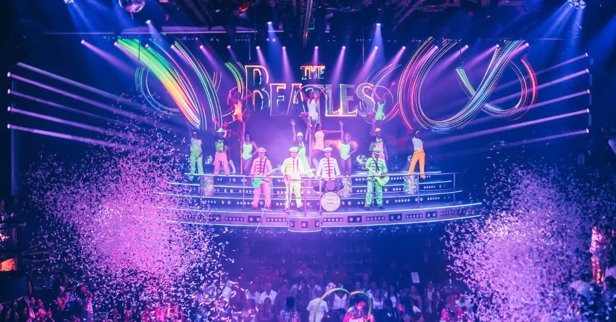 Dancers in bright costumes perform on a vibrant stage with neon lights, confetti, and cheering crowd at Coco Bongo night club.