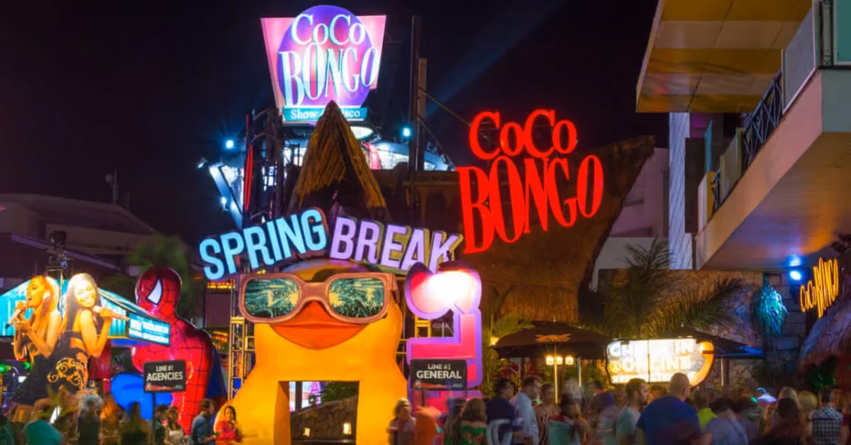 Coco Bongo night club entrance at night, red signs, yellow “Spring Break” display with sunglasses, colorful lights, lively crowd.