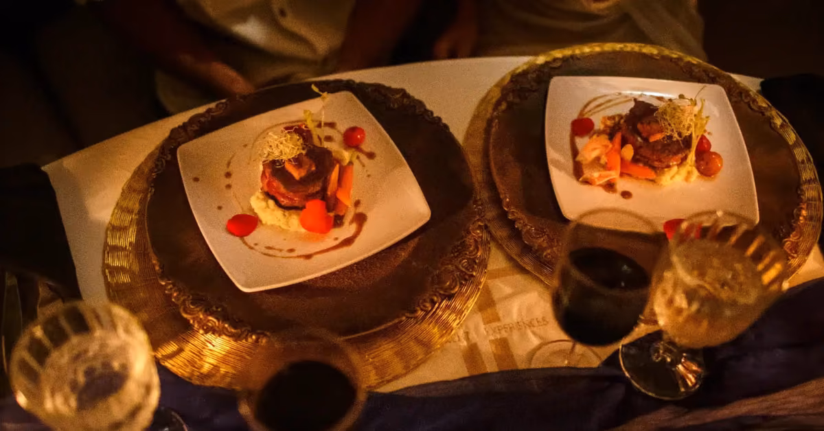 Two plates of gourmet food and glasses of wine sit on a table with ornate chargers, creating a warm, inviting atmosphere.