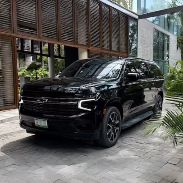 A black Chevrolet SUV is parked on a stone driveway before a modern glass and wood building, surrounded by greenery.