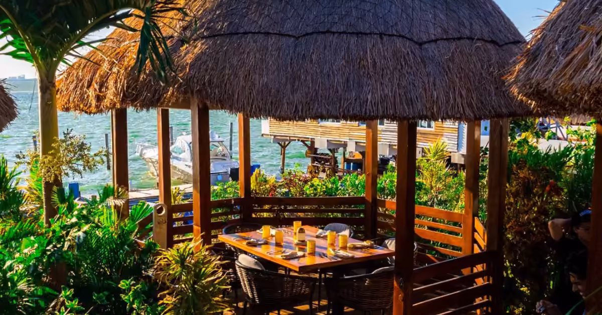 Fred’s Restaurant patio with thatched huts, lush greenery, and views of boats and docks on a sunny tropical waterfront.