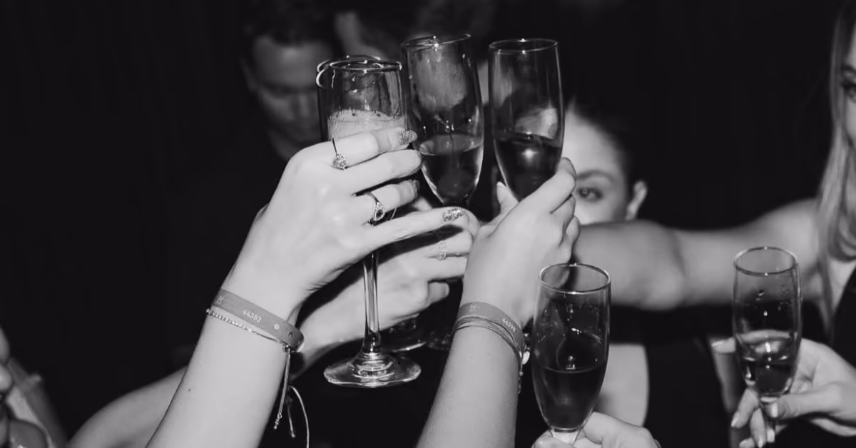 People clink champagne glasses in a toast at H Roof night club, hands and drinks highlighted against a dark background.