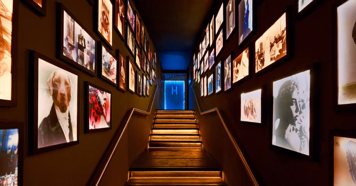 A dim stairway with glowing steps and lit photo frames on both walls leads to a blue-lit doorway at the top.