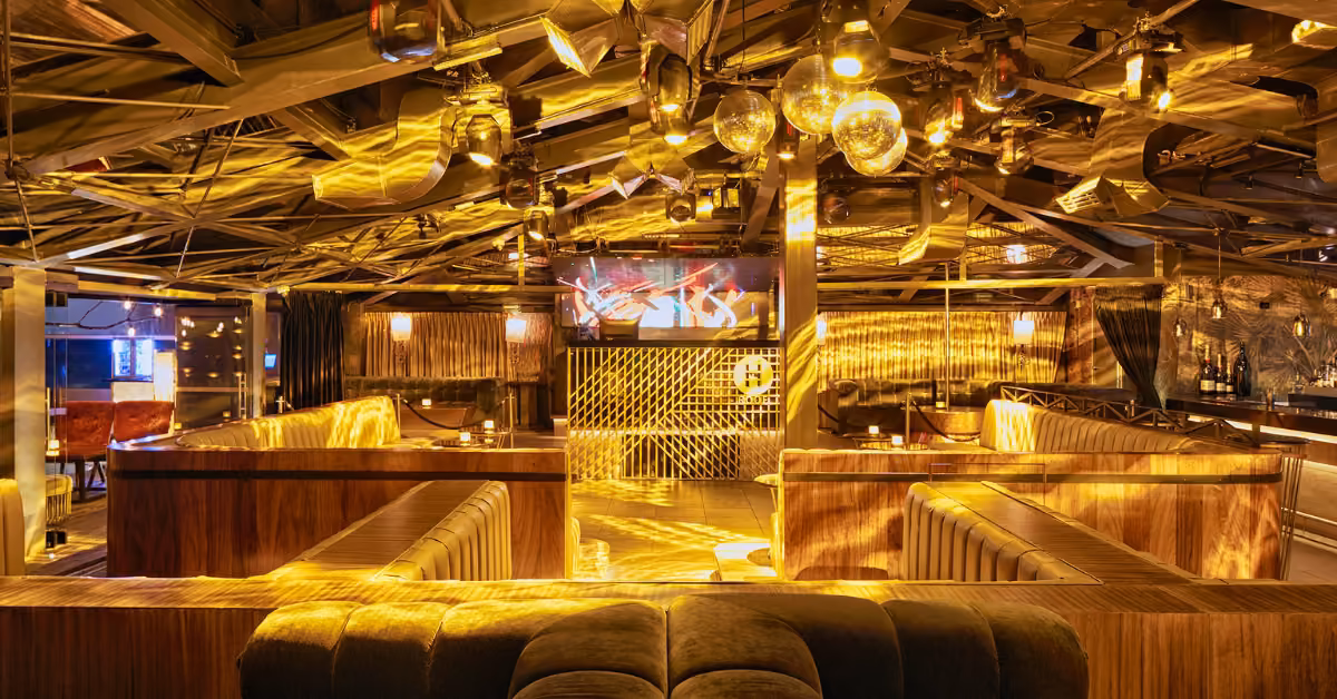 Night club interior with golden lighting, plush booths, disco balls overhead, and a central dance floor creates an energetic vibe.
