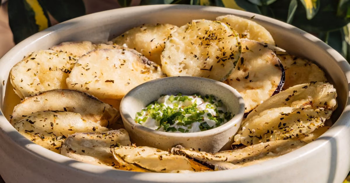 Crispy baked potato slices with herbs and creamy dip topped with green onions, served in a bowl at Ilios Restaurant.