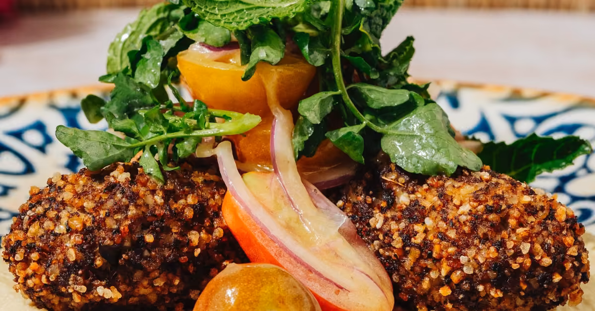 Golden croquettes topped with fresh greens, red onions, and yellow tomatoes on a patterned plate at Ilios Restaurant.