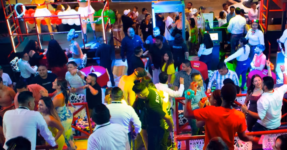 People dance, chat, and relax under colorful lights at La Vaquita Night Club, with festive decor and visible security staff.