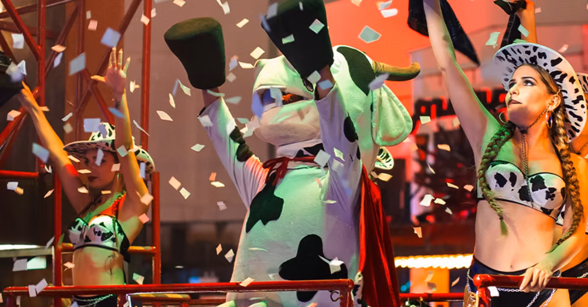 People in cow costumes celebrate on stage at La Vaquita Night Club as confetti falls amid bright lights and lively energy.