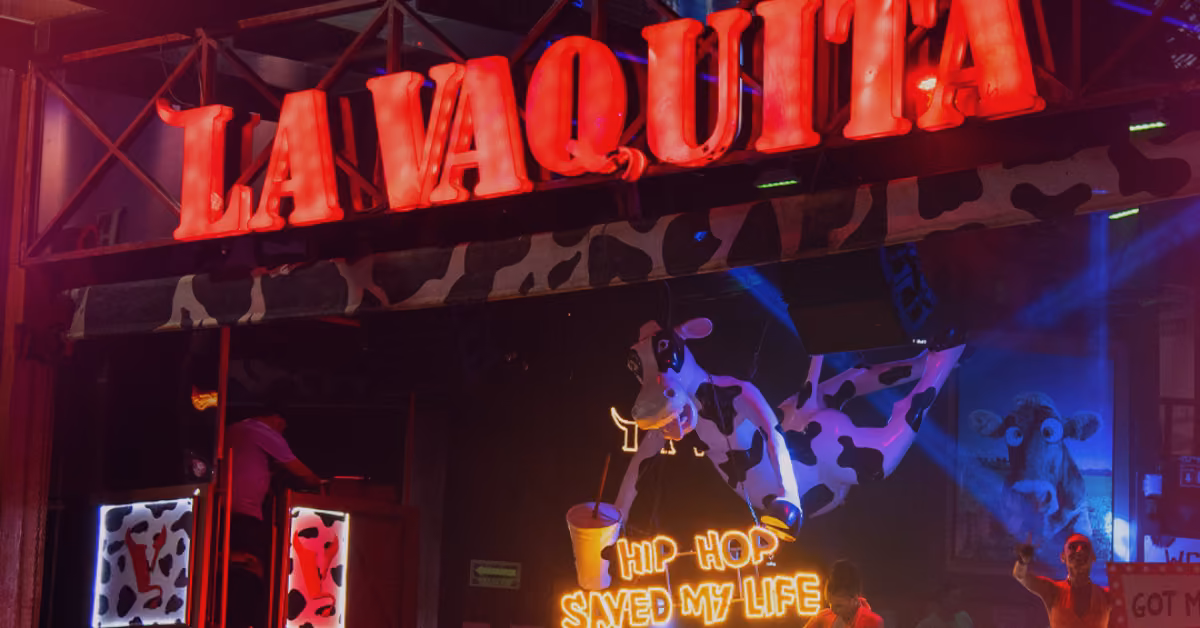 Neon La Vaquita sign above a night club entrance with cow patterns, cow figure, and “Hip-Hop Saved My Life” in neon below.