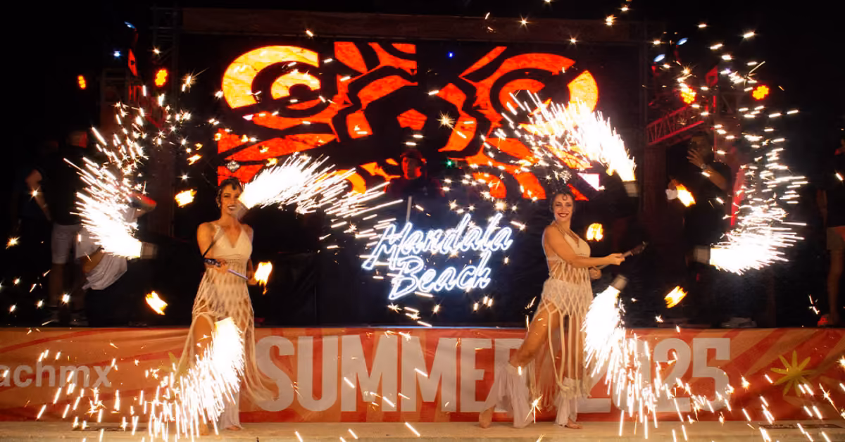 Two costumed performers spin flaming batons, sending sparks flying on stage at Mandala Beach Club with SUMMER 2025 signage.