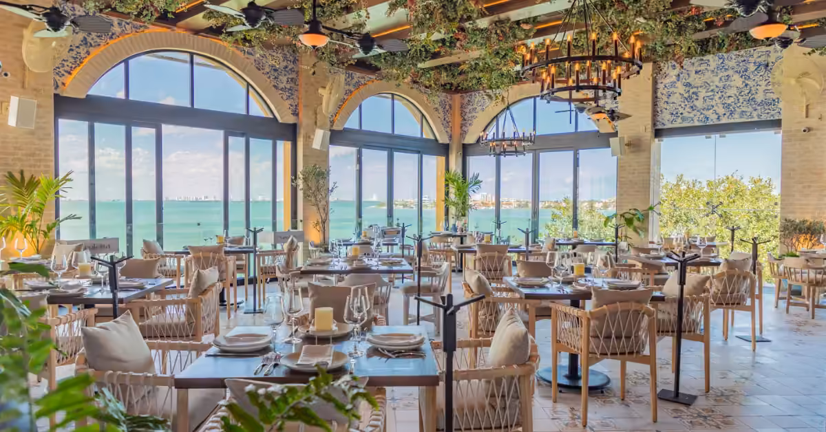 Nicoletta Restaurant features arched windows with lagoon views, filled with natural light, greenery, and wooden furnishings.