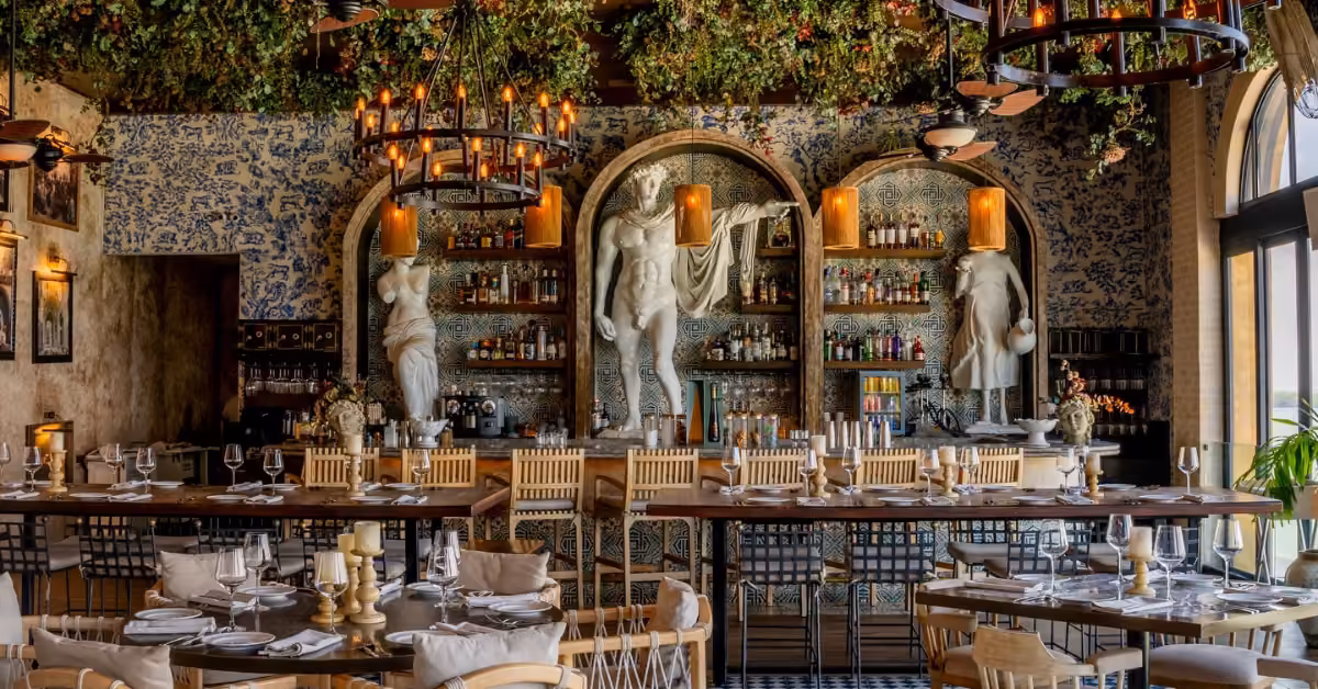 Nicoletta restaurant with elegant tables, chandeliers, lush ceiling greenery, and classical statues behind a decorative bar.