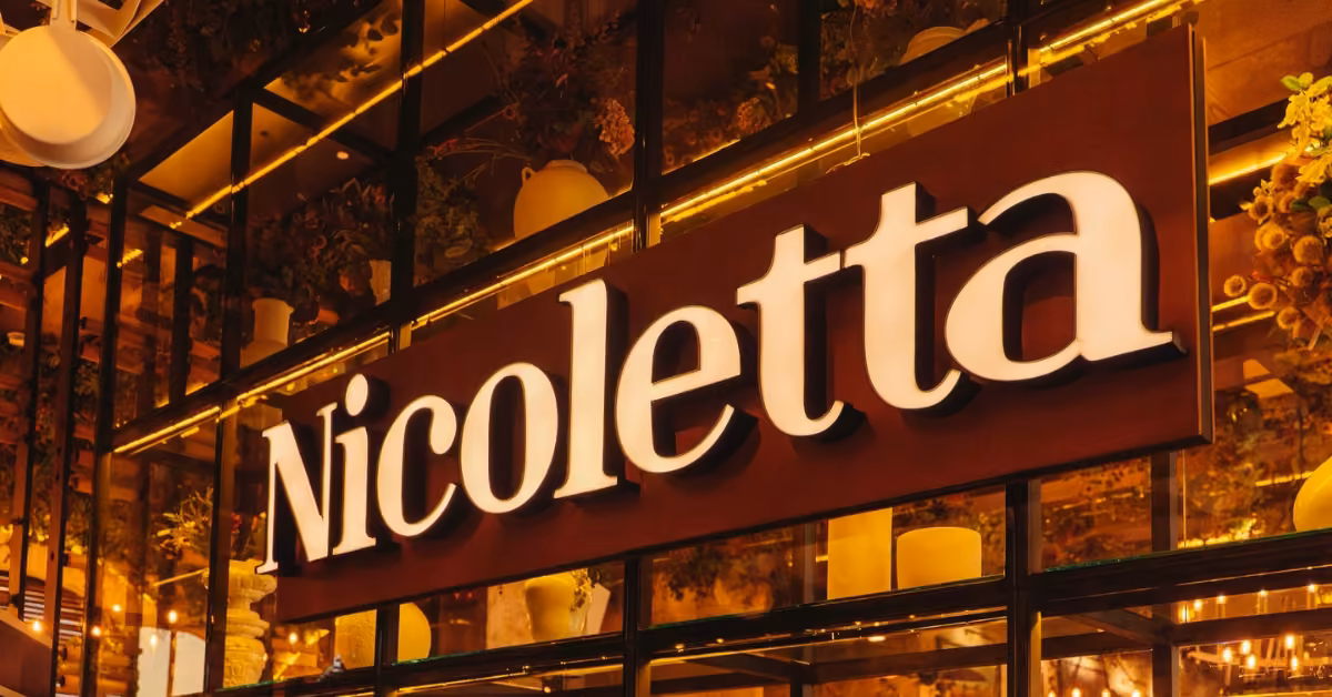 Nicoletta restaurant sign glows with warm yellow light and decorative plants, creating a cozy, inviting atmosphere.
