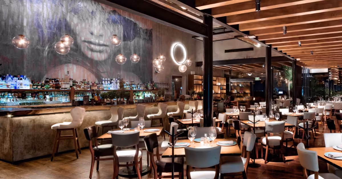 Modern restaurant with wooden beams, round lights, mural of a face, elegant tables, and a warm, inviting atmosphere.