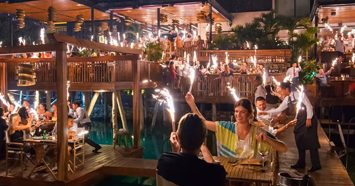 Nighttime celebration at Rosa Negra with sparklers, wood accents, tropical plants, and festive lights. The mood is joyful.