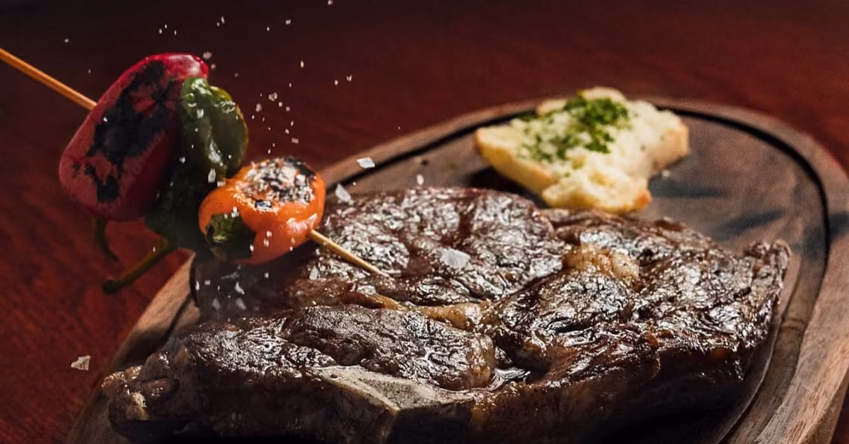 Grilled steak on a wooden platter with skewered peppers, seasoned bread, and a sprinkle of salt at Rosa Negra.