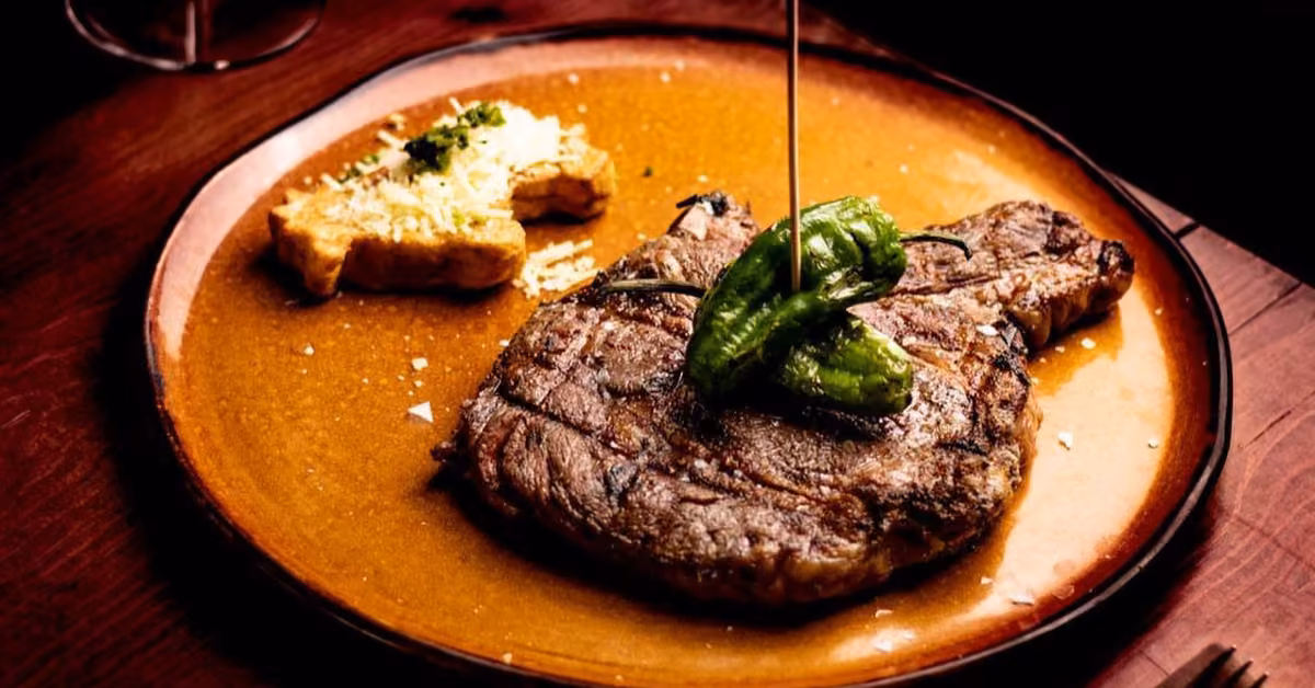 Grilled steak with green peppers and cheesy potatoes on a brown plate under warm lighting, ready to be enjoyed.