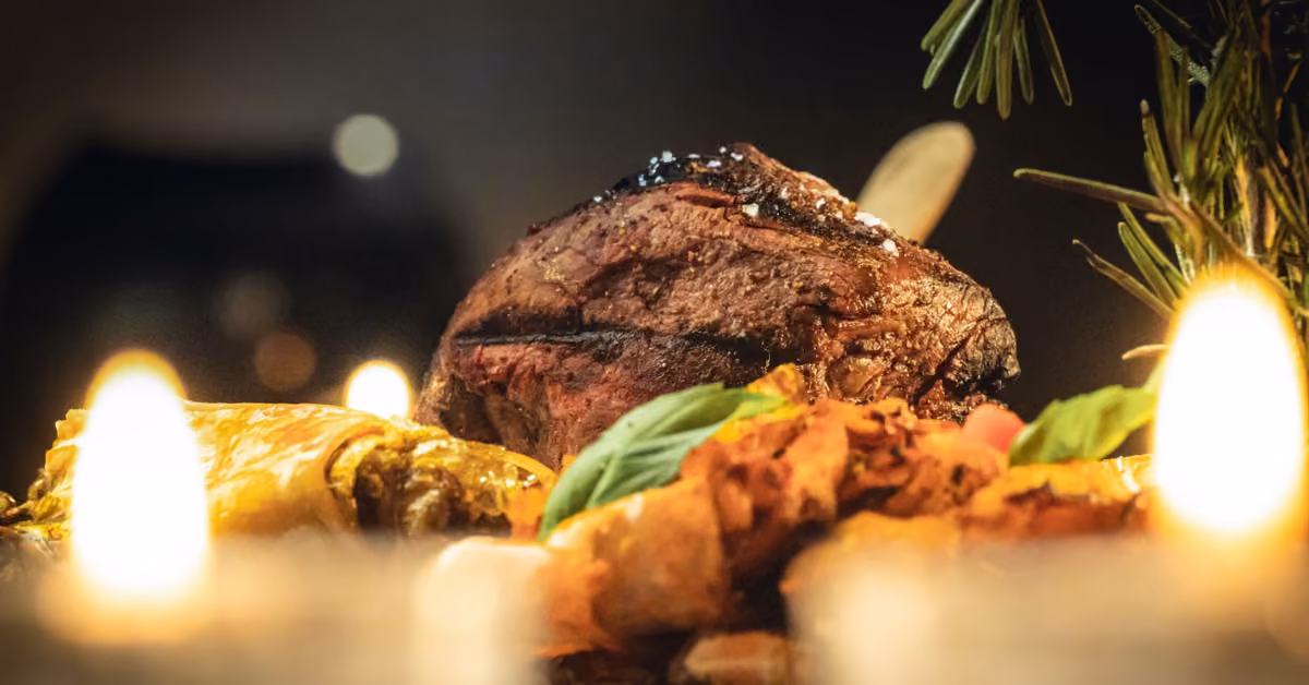 Grilled steak, baked rolls, and fresh basil on a warmly lit table with candles at Taboo Restaurant.