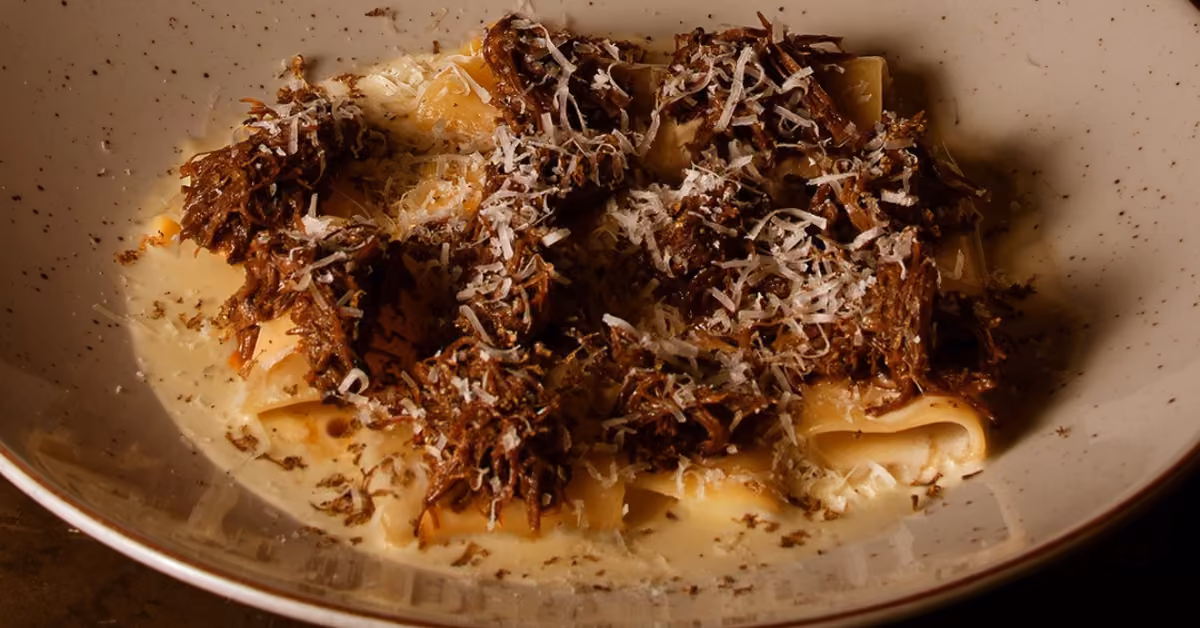 Pasta ribbons with braised meat and grated cheese in a creamy sauce, served in a shallow bowl from Taboo Restaurant.