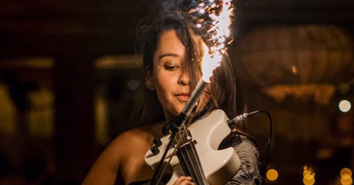 A woman plays electric violin with a sparkler at the tip, sending sparks in the dimly lit atmosphere of Taboo Restaurant.