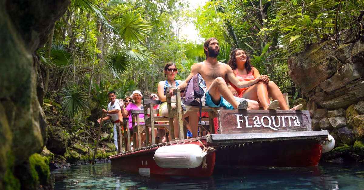 People ride a wooden raft called Flaquita, drifting on clear water through Xcaret’s vibrant jungle and rocky landscape.