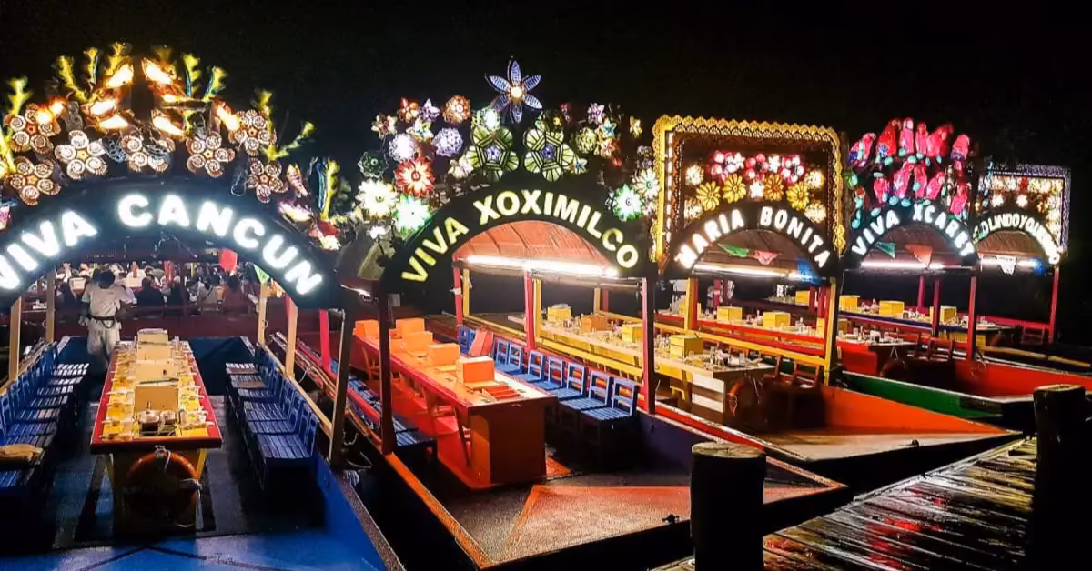 Brightly lit boats with festive arches and names like Viva Cancun are docked at night, tables set for a lively party.
