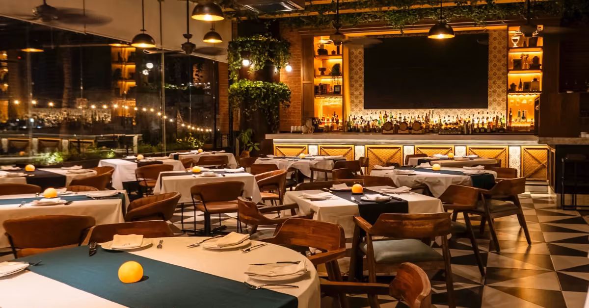 Cozy Bodega Argentina restaurant with set tables, wooden chairs, warm lighting, candles, bar, greenery, and decorative tiles.