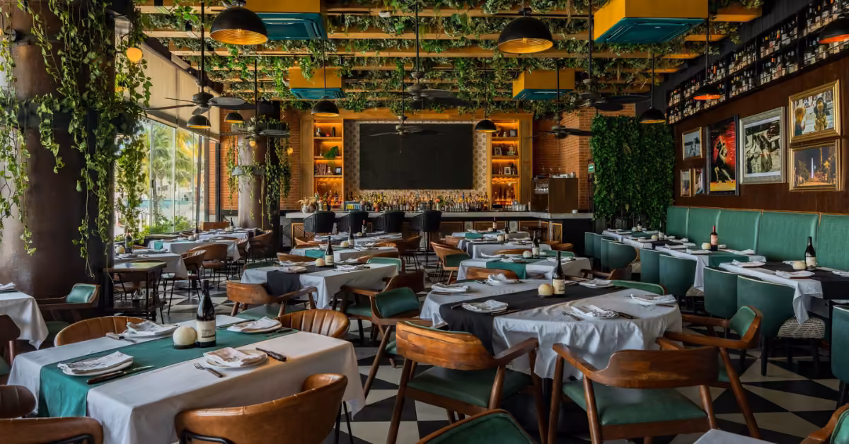 Argentinian restaurant with wooden tables, green seats, hanging plants, framed art, and a leafy ceiling above the bar.