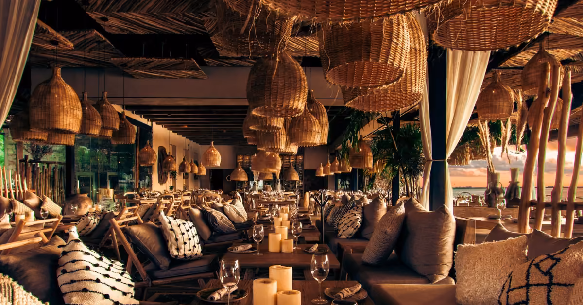 Chambao restaurant with wicker lamps, wood furniture, soft seating, candles, warm light, and sunset views in a relaxed setting.