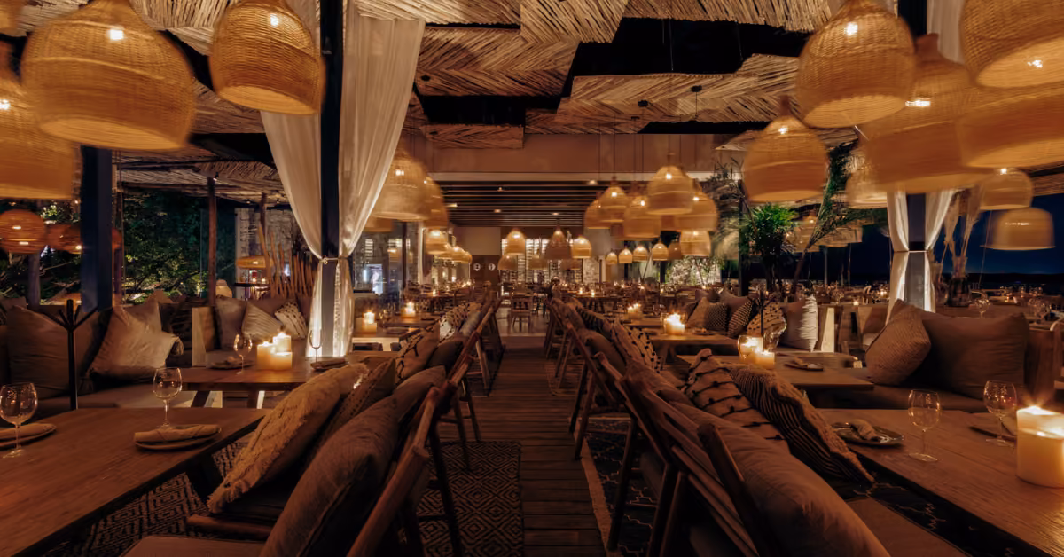 Chambao Restaurant glows with candles, wood tables, cushioned chairs, wicker lamps, and draped curtains for a cozy dinner.