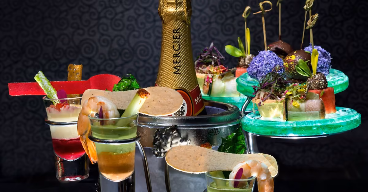 Colorful appetizers, creative drinks, and a chilled Mercier champagne bottle set against a dark, stylish background.