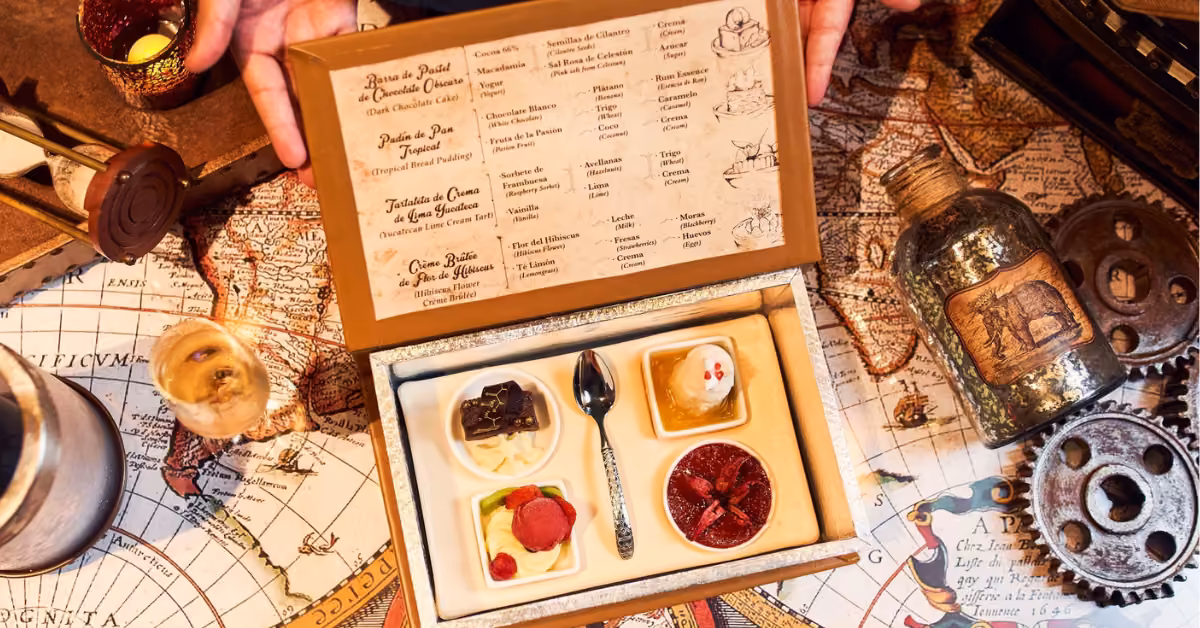A tray with four desserts, a spoon, and menu sits on a map table with vintage props evoking an adventurous atmosphere.
