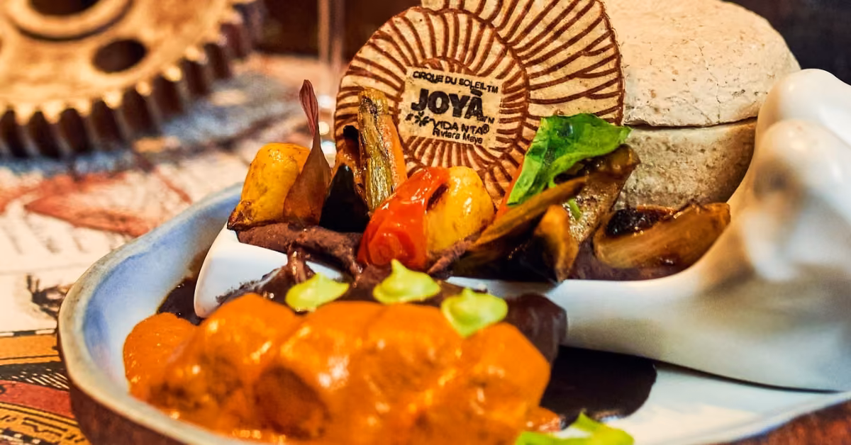 Vegetables, creamy orange sauce, and a bread dome with a Cirque du Soleil JOYA wafer on a white hand-shaped plate.