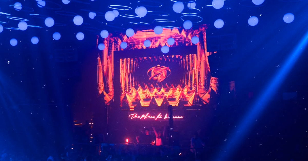 D’Cave Night Club with a large LED screen of orange patterns, glowing ceiling orbs, and people dancing below.