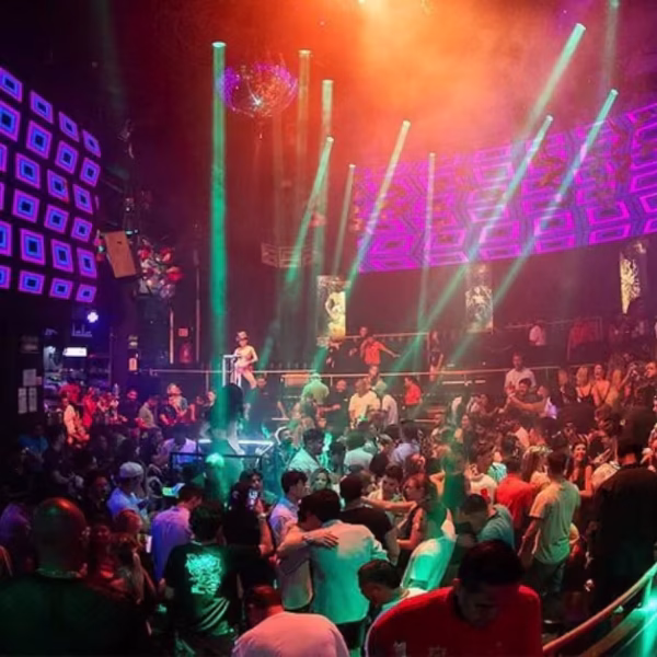 A lively nightclub with colorful lights, people dancing and chatting, and glowing geometric patterns on the walls and ceiling.