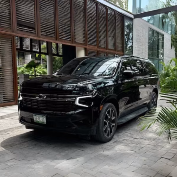 A black Chevrolet SUV is parked on a stone driveway before a modern glass and wood building, surrounded by greenery.