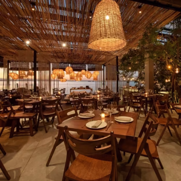 Cozy restaurant with wooden tables, chairs, wicker lights, and a woven ceiling; tables set for a warm, inviting meal.