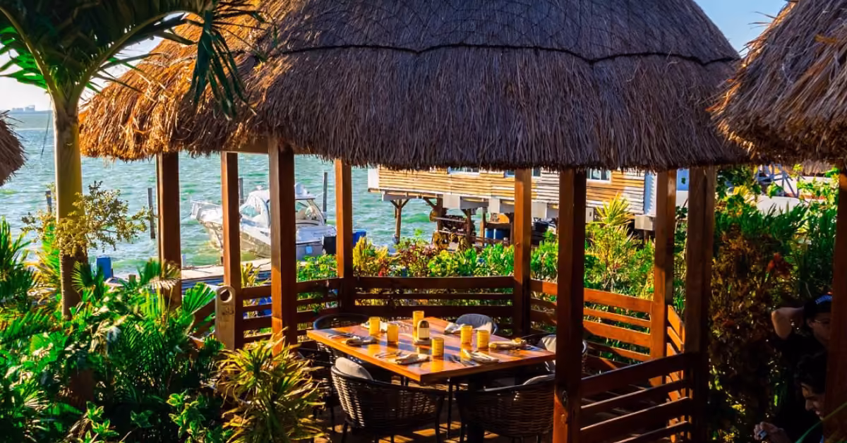 Fred’s Restaurant patio with thatched huts, lush greenery, and views of boats and docks on a sunny tropical waterfront.
