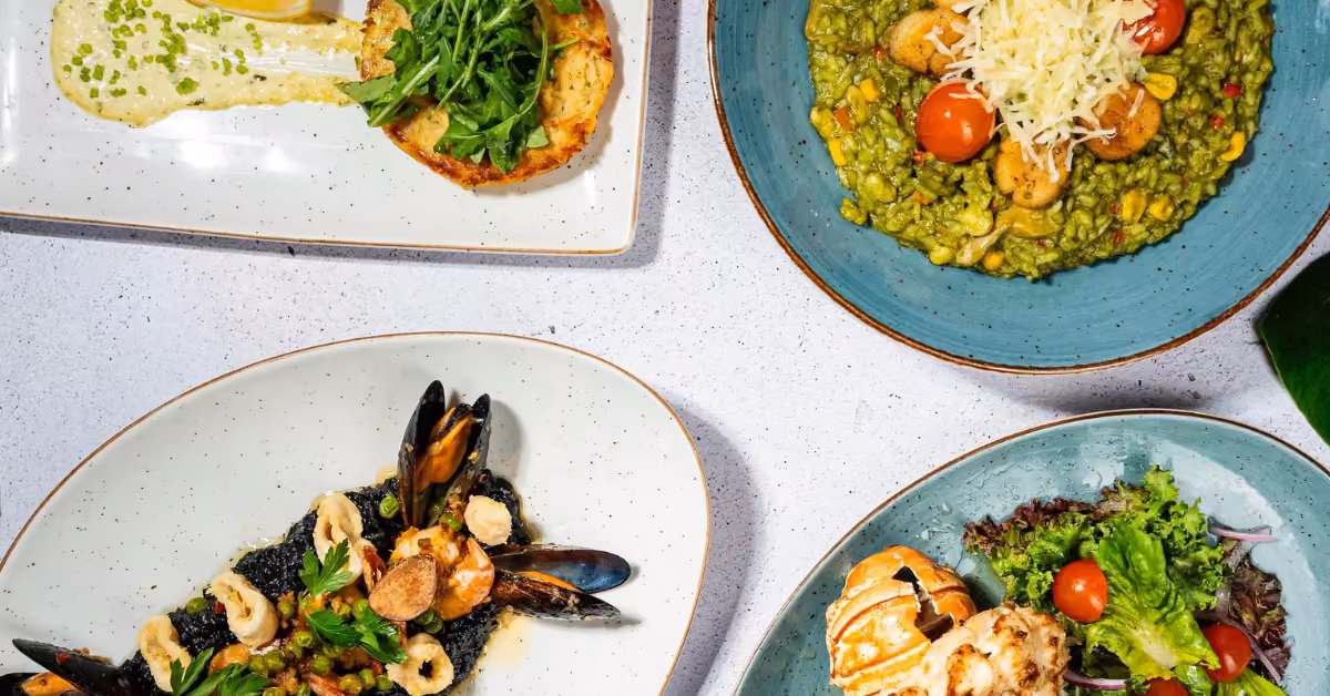 Four artfully arranged plates with salad, seafood, risotto, and shrimp sit on a white table at Fred’s Restaurant.