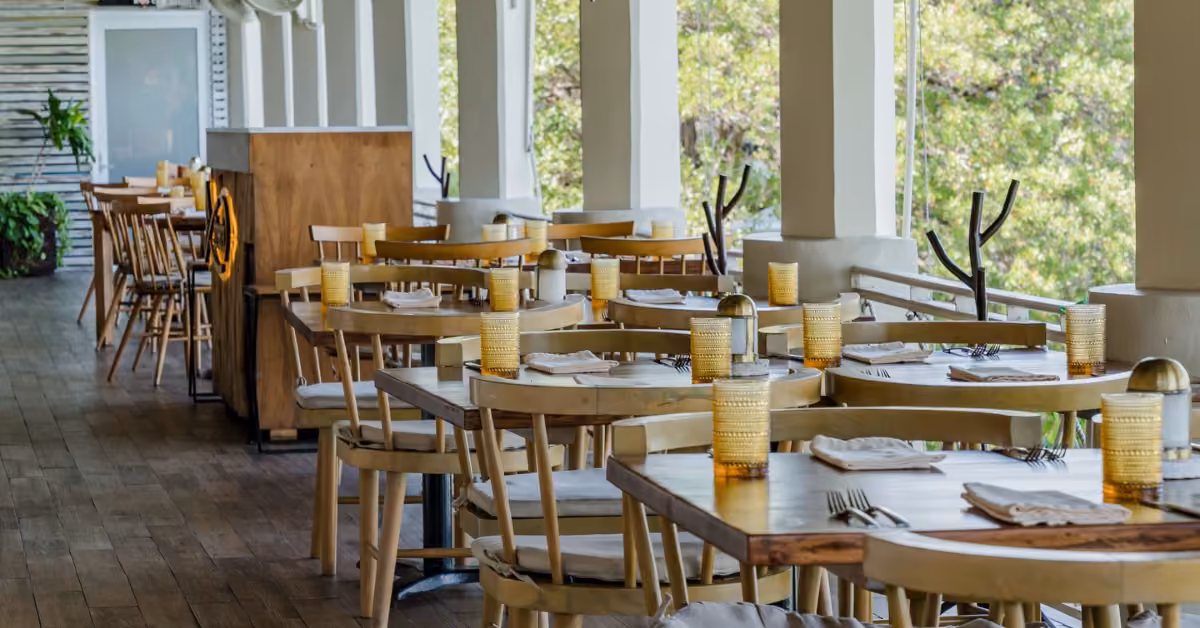 Fred’s restaurant patio with wooden tables set with yellow glasses and napkins, shaded by greenery in the background.