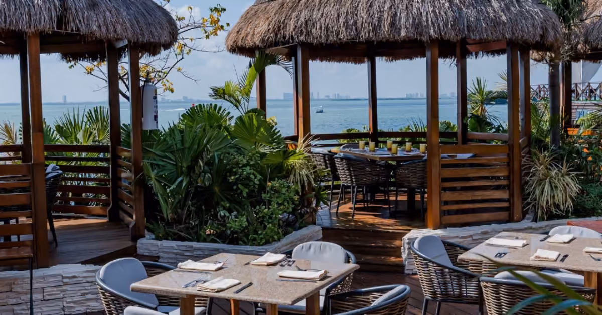 Outdoor dining at Fred’s under thatched gazebos, surrounded by tropical plants and water views with the city skyline beyond.