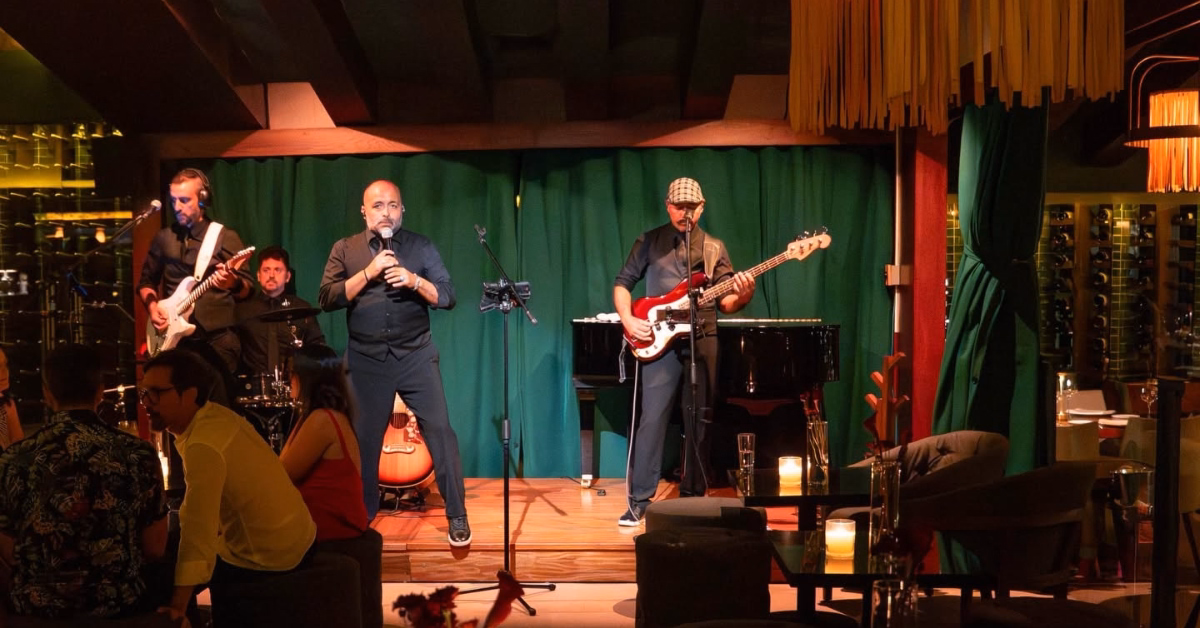 A five-member band plays onstage before a green curtain as candlelit tables and a cozy audience fill Harry’s Bar.