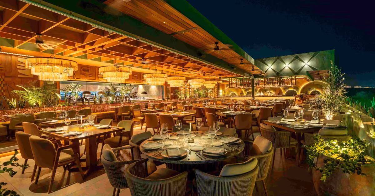 Rooftop dining at Harry’s Restaurant with warm lighting, modern decor, glassware tables, plush chairs, plants, and chandeliers.