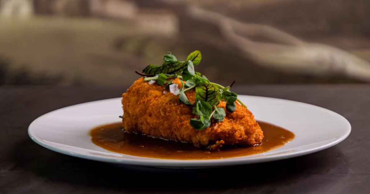 Golden breaded meat on a white plate with brown sauce, topped with fresh herbs and microgreens at Harry’s Restaurant.