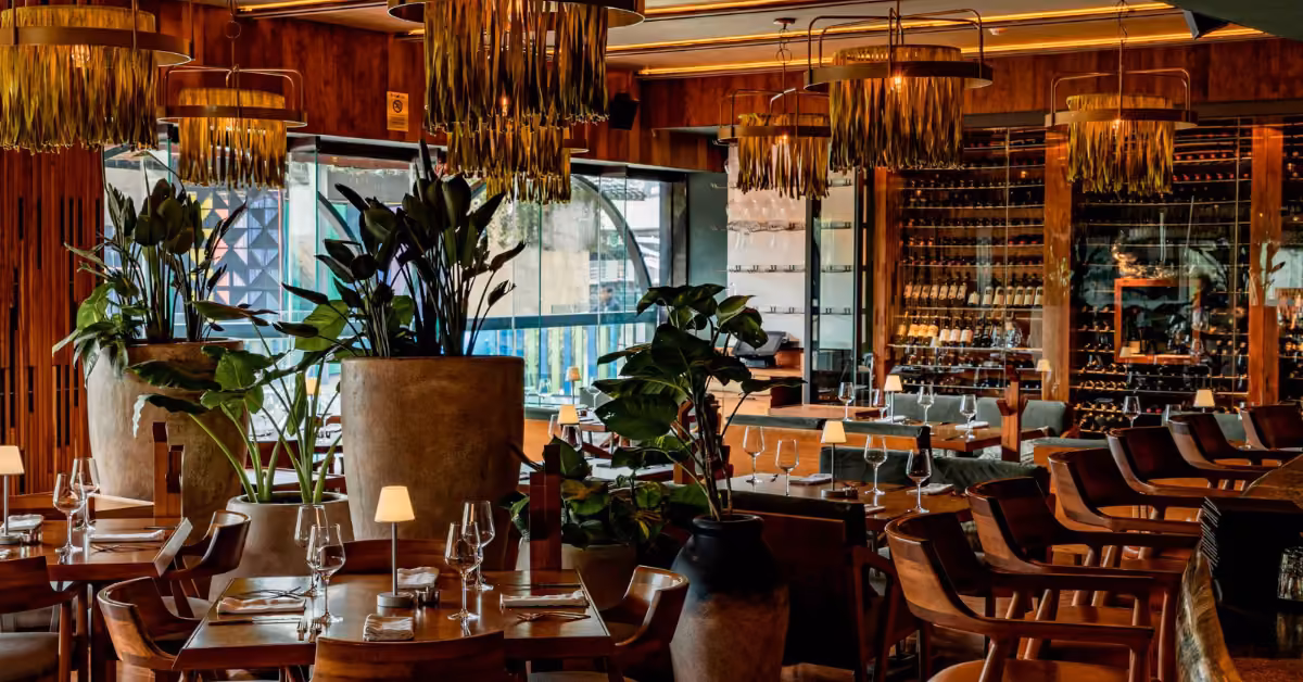 Harry’s Restaurant interior features wooden tables, lush plants, modern lights, a wine wall, and elegant table settings.